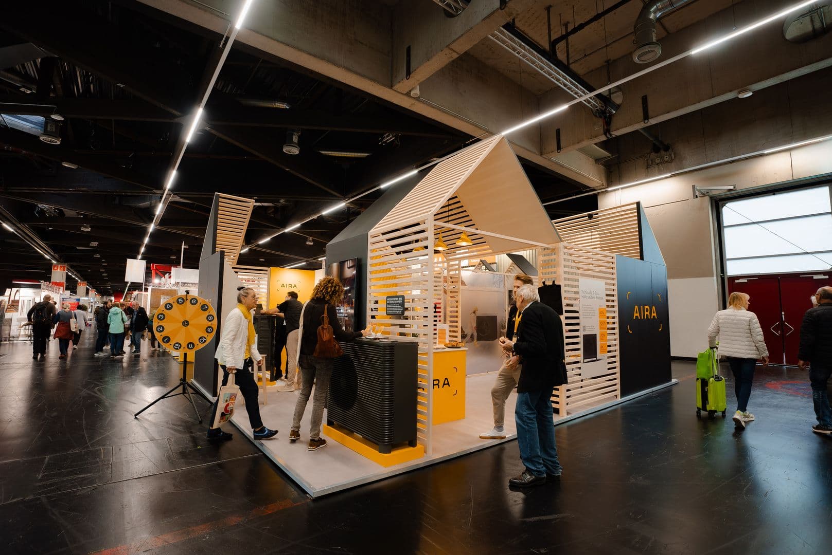 belebter Messestand mit Wärmepumpe, Glücksrad und Kunden