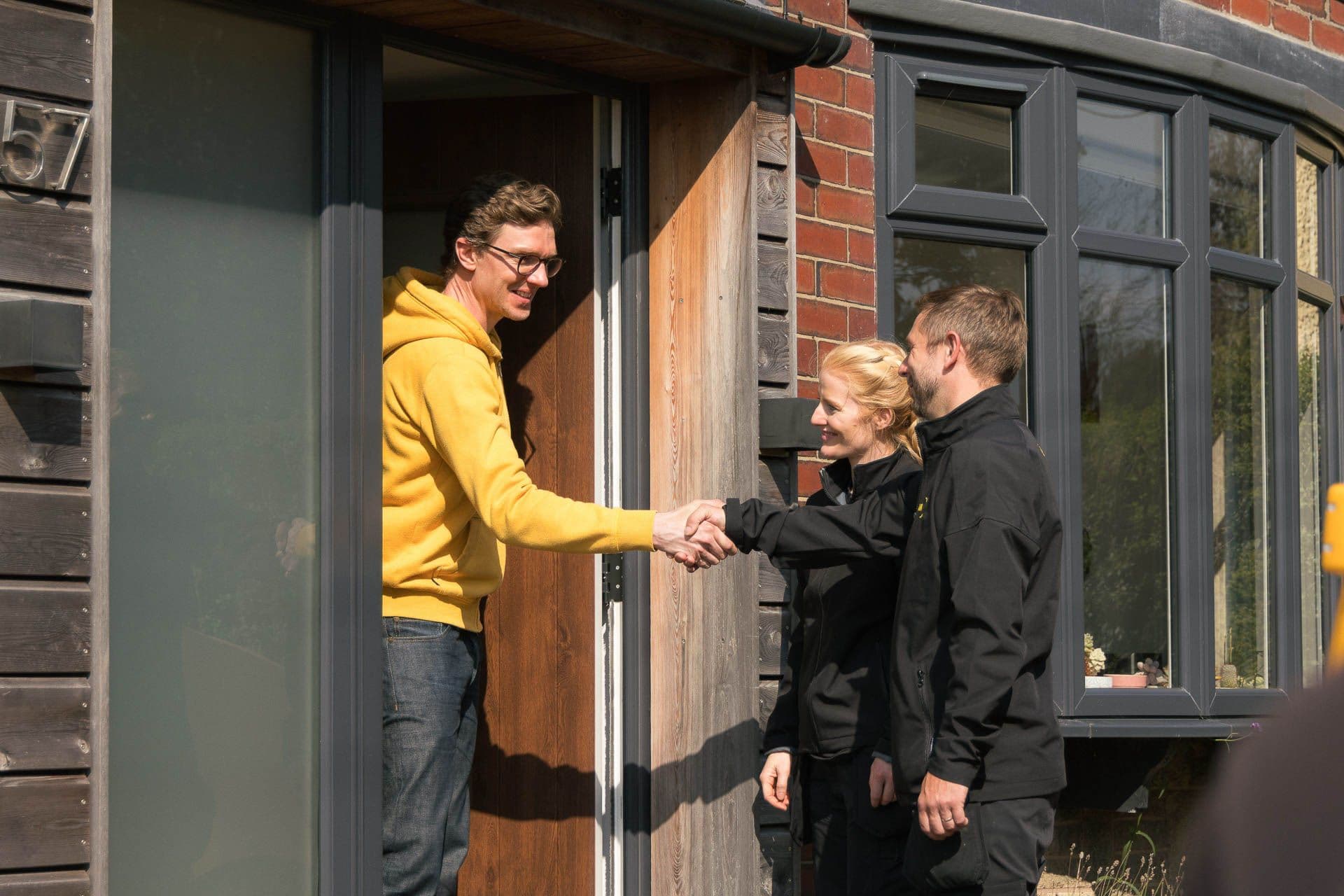 Man shaking hands with two Aira Clean Energy Technicians ahead of an Aira Heat Pump installaition at his home