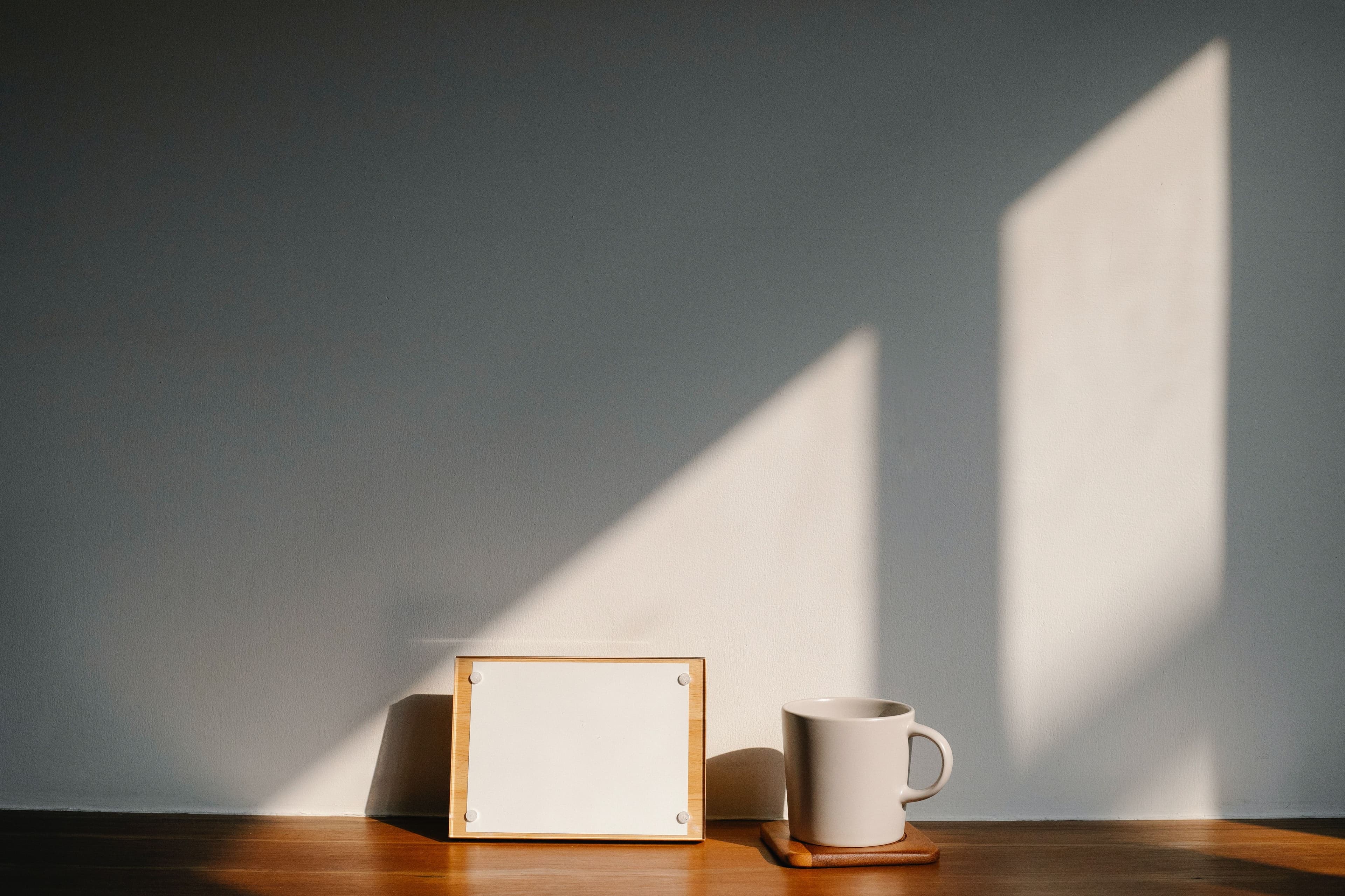 Notice board and a mug on a wooden table. Light shining in through windows.