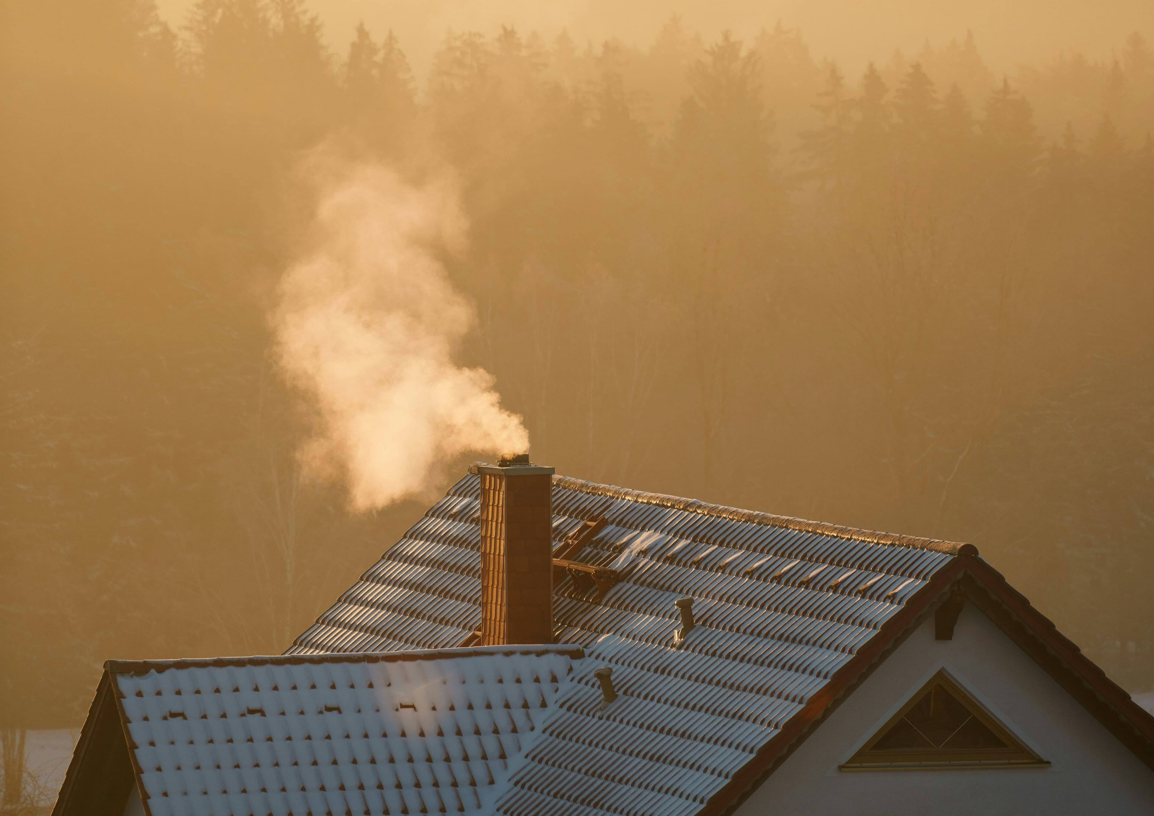Ein Dach von einem Haus bei Abendsonne mit einem Schornstein aus dem es dampft