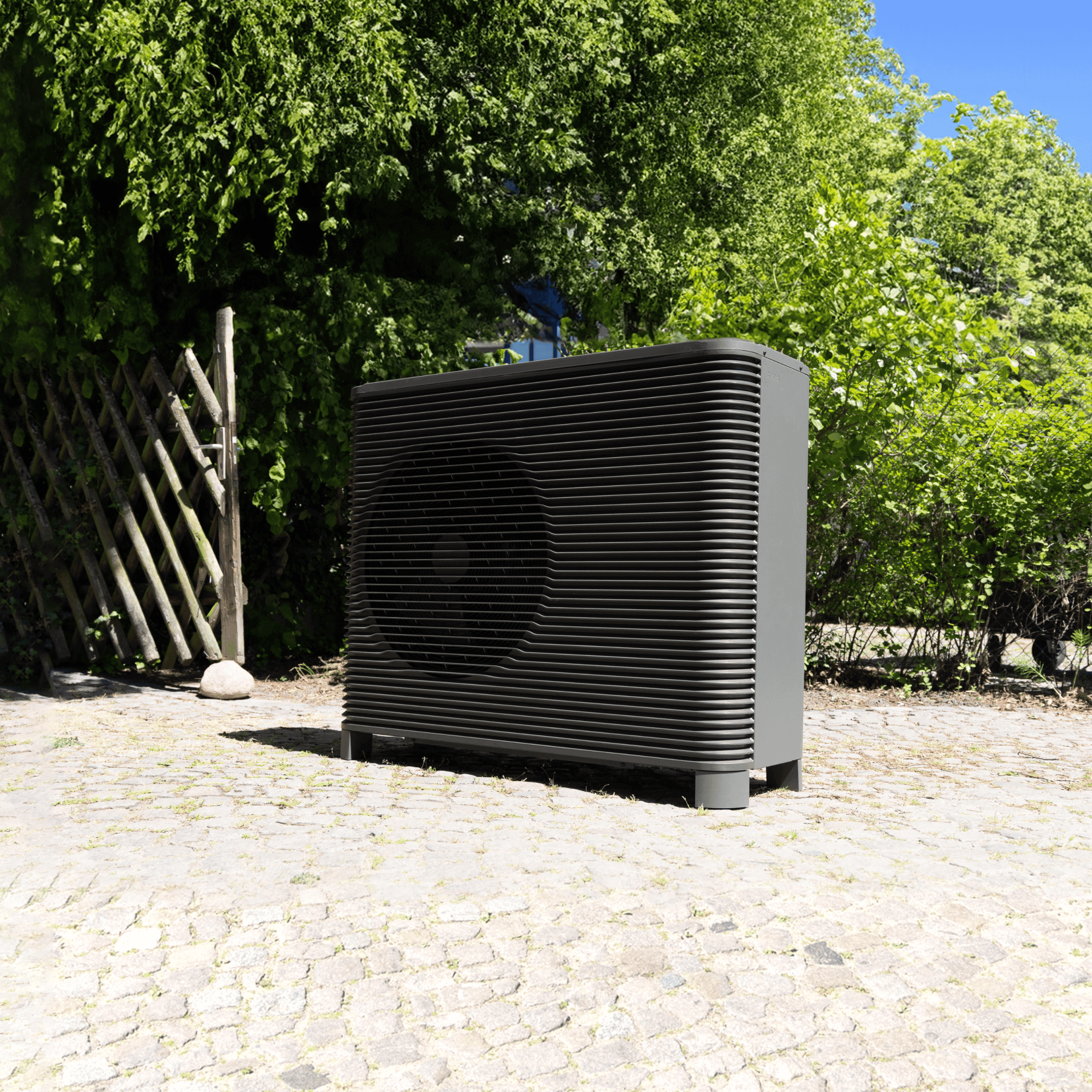 Front view of an Aira 8kW air source heat pump placed on some cobbled paving with trees in the background